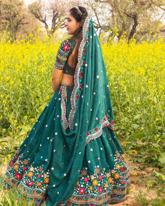 Woman in a traditional green embroidered outfit standing in a field of yellow flowers.