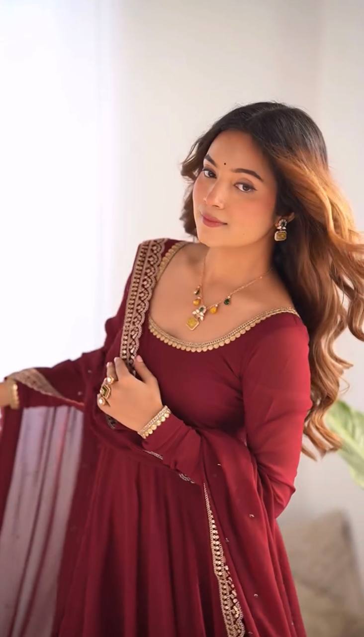 Woman in a red traditional outfit with gold details, holding a dupatta.