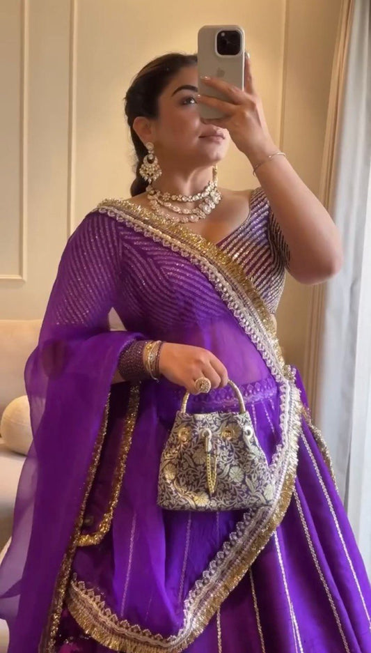Woman in a purple traditional outfit with gold details, holding a matching handbag.