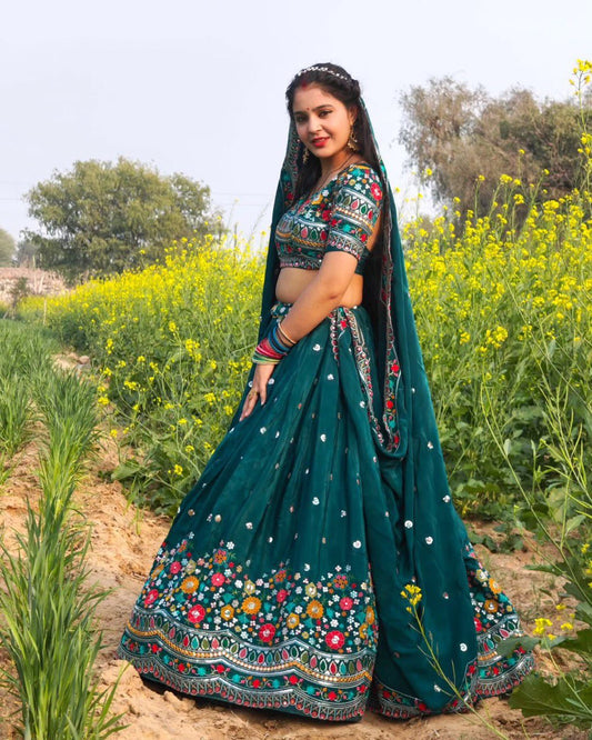Woman in a traditional green embroidered outfit standing in a field with yellow flowers.