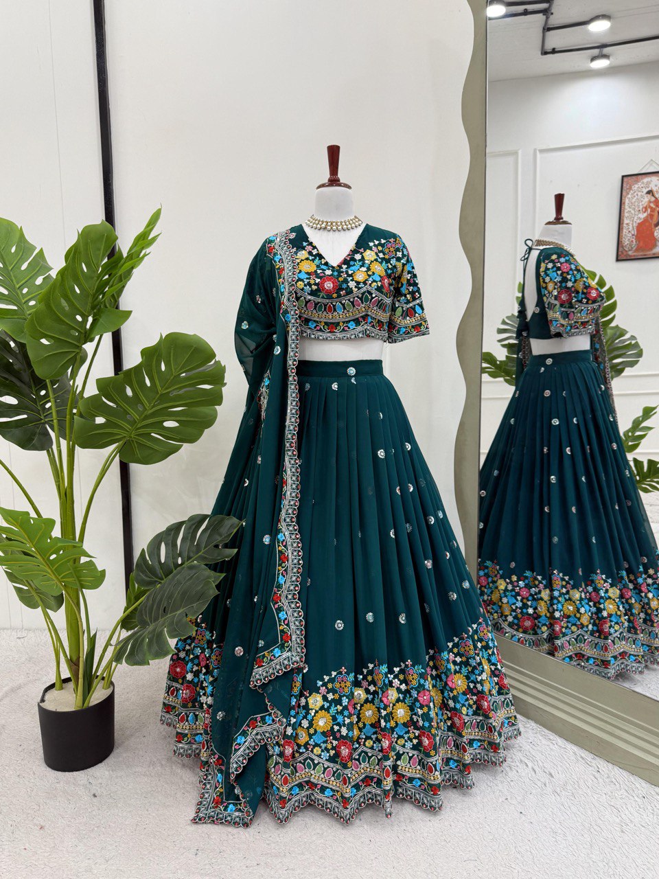 Teal embroidered lehenga with colorful details on a mannequin against a white wall.